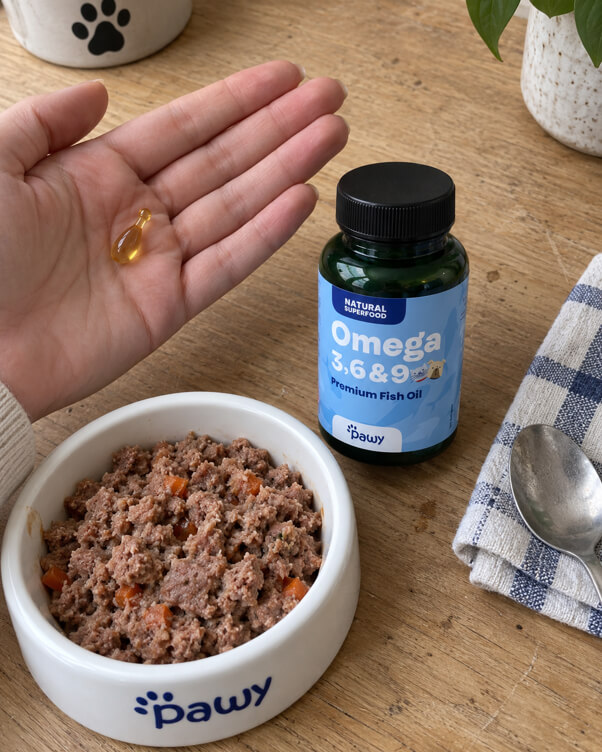 An omega-3 capsule in a hand next to the bottle and a Pawy bowl
